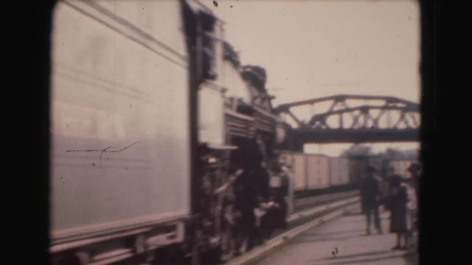 1975 8mm home-movie frame showing a train passing a Washington, DC station platform with several distant figures nearby.
