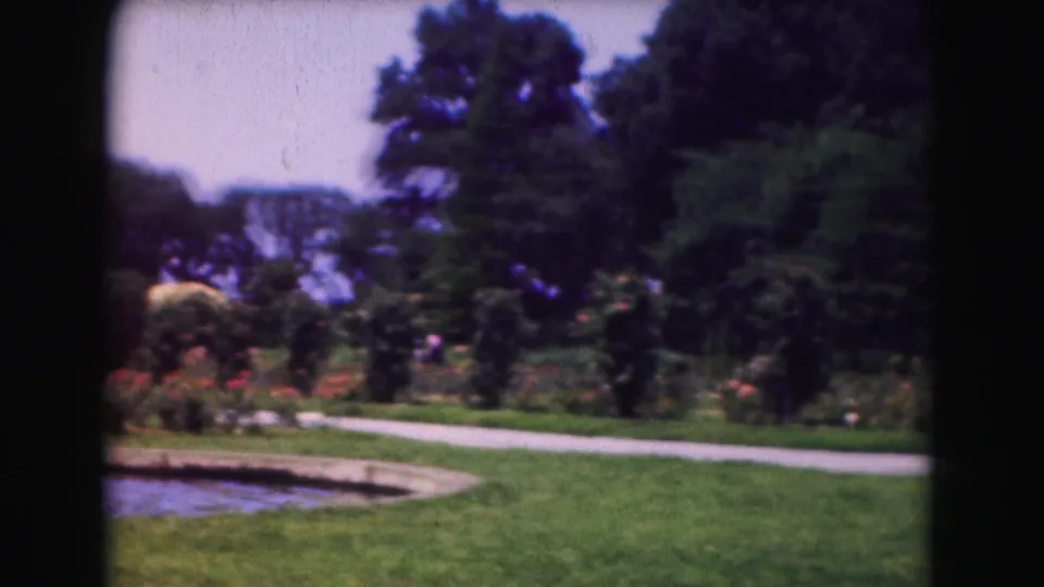 1975 Washington DC 8mm frame showing a landscaped garden with green lawn, curved paved path, pond edge, trees, and flower beds.