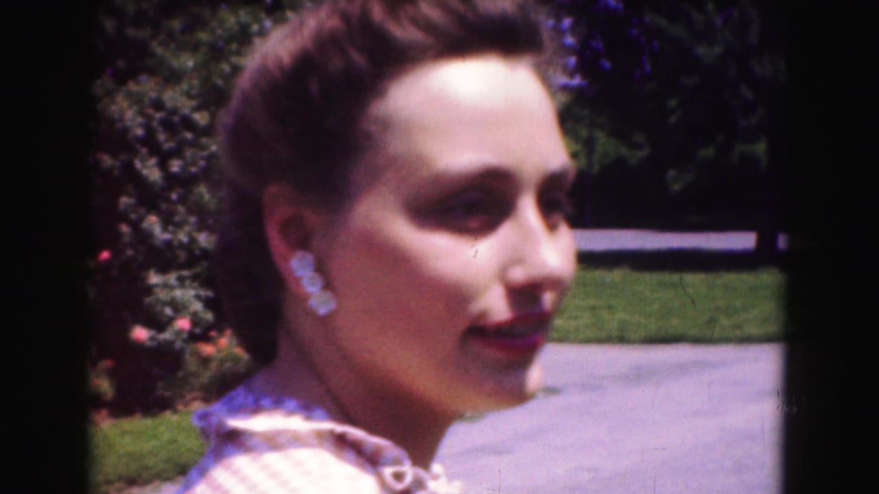 Young woman in a checkered blouse and earrings looks toward the camera in a Washington, DC garden, 1975.