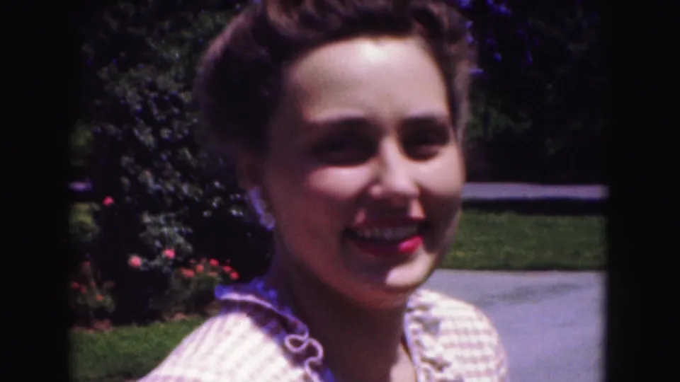 Smiling young woman faces the camera in a 1975 Washington, DC garden scene with lawn and shrubs behind her.