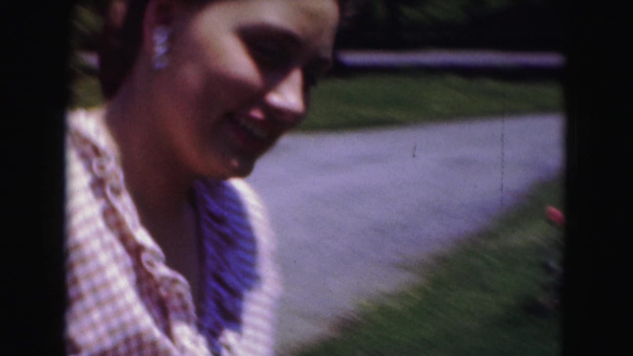 Woman in a checkered dress smiles near the camera outdoors.