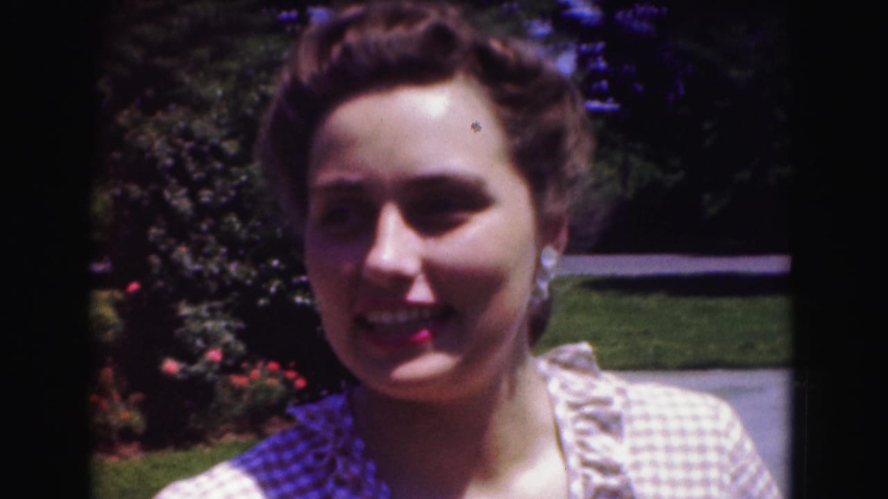 Woman in a checkered dress smiles with greenery behind her.