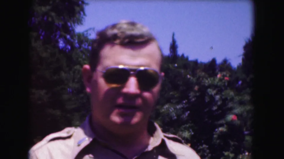 A man in aviator sunglasses and a tan uniform-style shirt faces the camera in 1975 Washington DC home-movie footage.