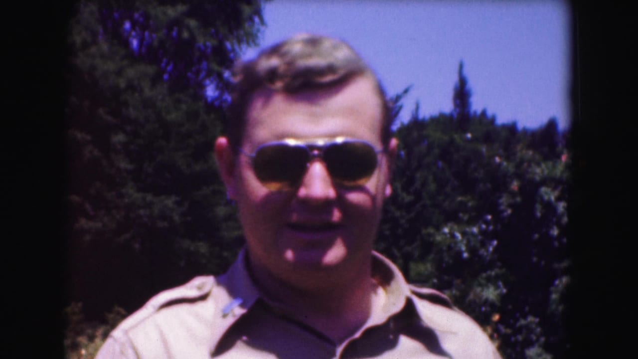 Adult man in aviator sunglasses and a khaki shirt faces the camera outdoors in 1975 Washington, DC home-movie footage.