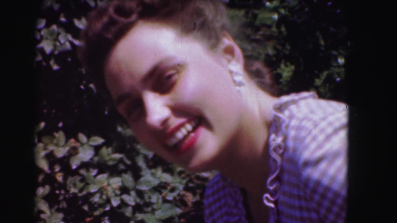 Smiling young woman in a checkered dress beside leafy greenery.