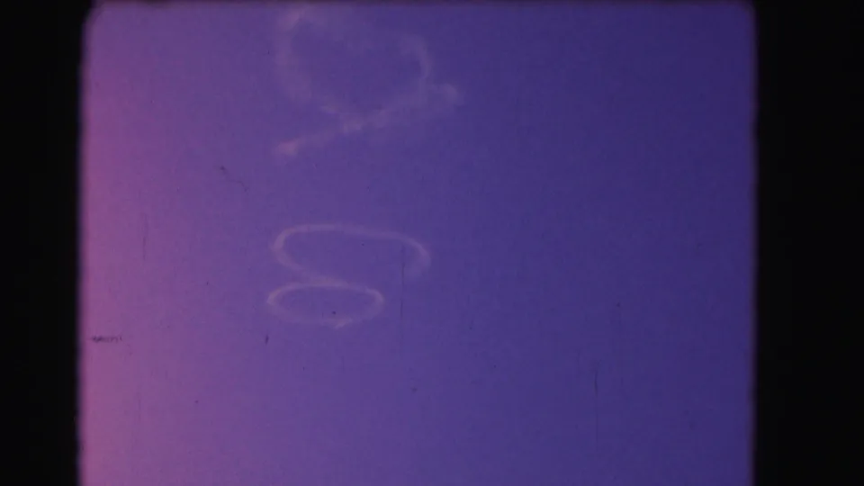 1975 Washington, DC 8mm frame showing faded blue-magenta exposure with dust, scratches, and dark film borders before the garden view appears.