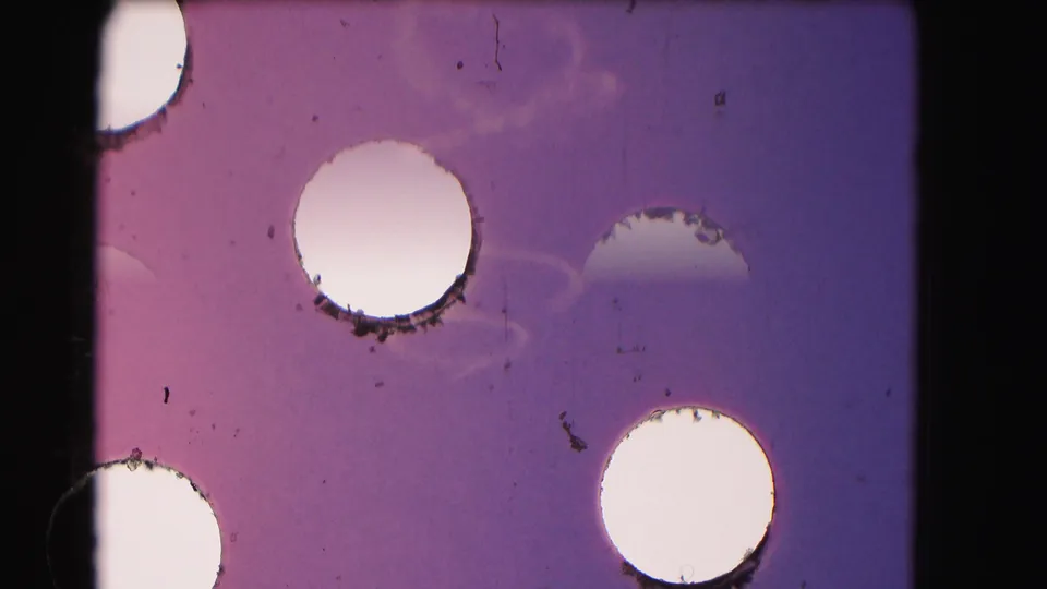 1975 8mm Washington, DC frame with overexposed circular marks, magenta-blue fading, dust, scratches, and visible film handling artifacts.