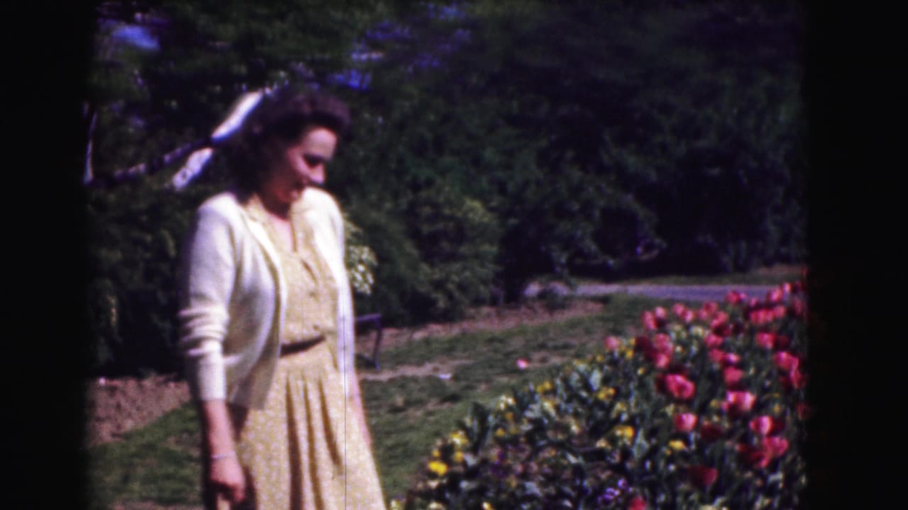 Woman in a yellow dress and white cardigan standing near tulips in a garden.