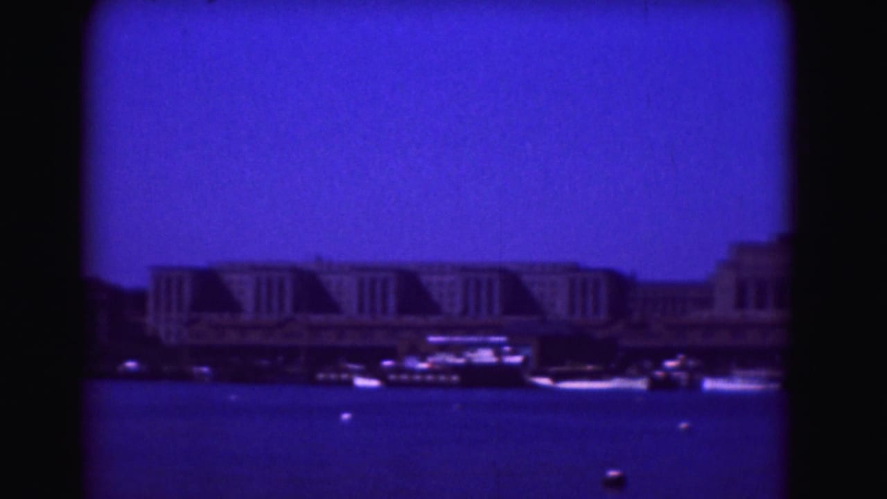 Waterfront buildings and boats across blue water in a dark-bordered 8mm frame.
