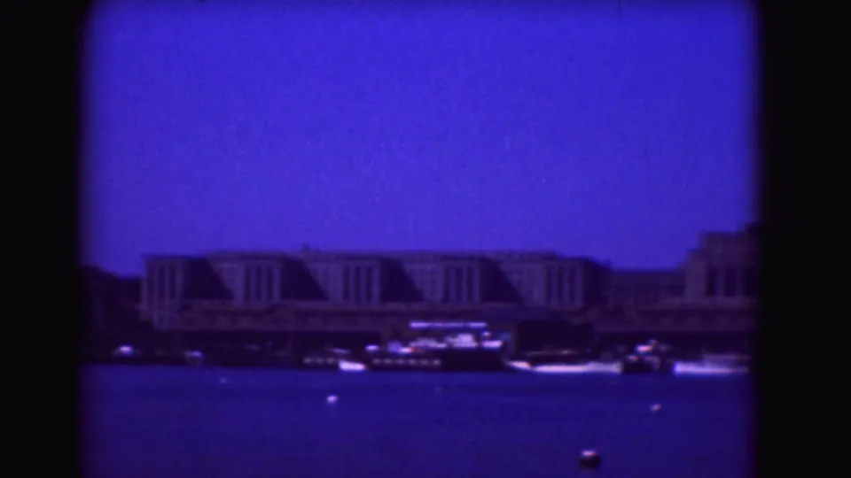 1975 Washington, DC waterfront view from across the Potomac River, with low buildings, boats, buoys, and heavy blue film color.