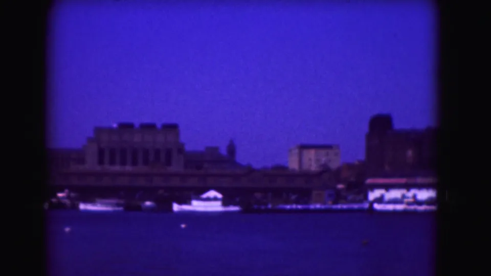 1975 Washington, DC waterfront frame with boats on the Potomac River, blocky shore buildings, blue sky, and visible 8mm frame edges.