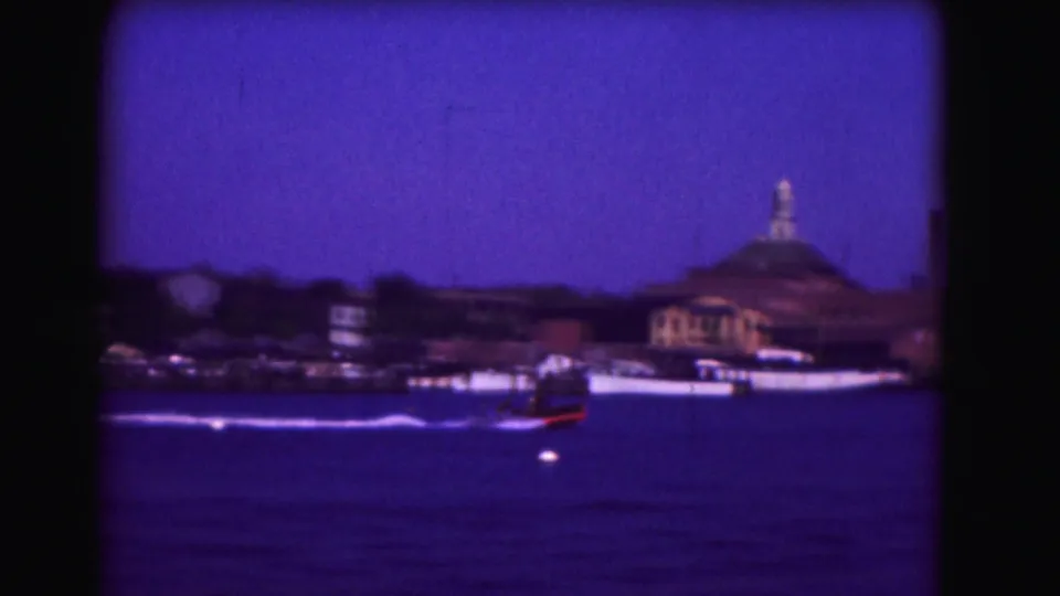Likely 1975 Washington, DC footage of a motorboat crossing the water before a domed shoreline structure and trees.