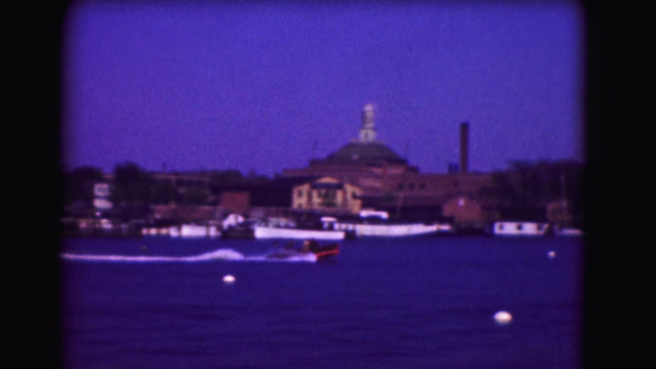 1975 Washington, DC 8mm waterfront view with a speedboat crossing the water and a domed structure beyond docked boats.