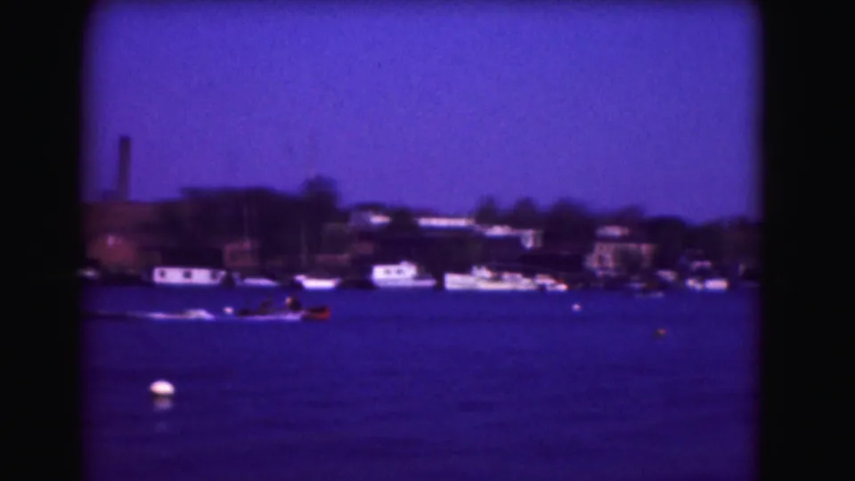 1975 Washington, DC 8mm harbor view with a speedboat crossing in front of moored boats and shoreline buildings.