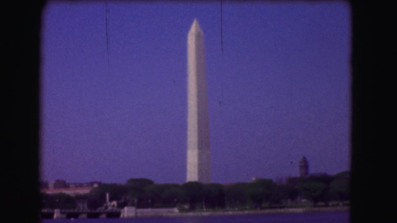 Washington Monument rising above a tree-lined shore across the water.
