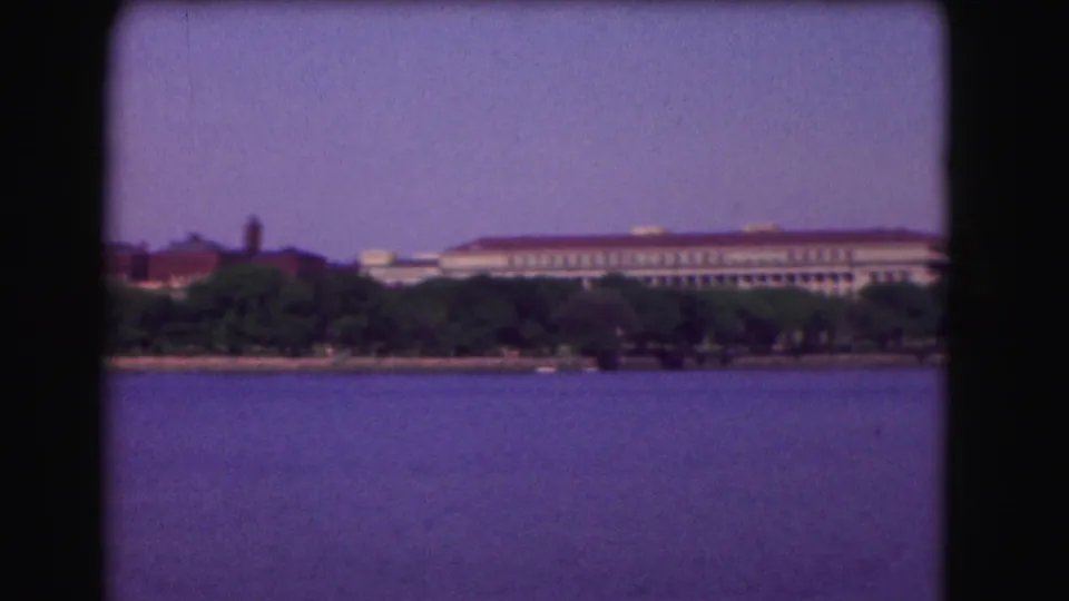 1975 Washington, DC frame showing a broad river foreground and a large distant institutional-looking building behind trees.
