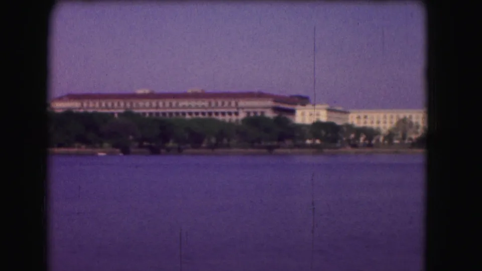 1975 Washington, DC home-movie view of a distant waterfront building complex, trees, and open river water.