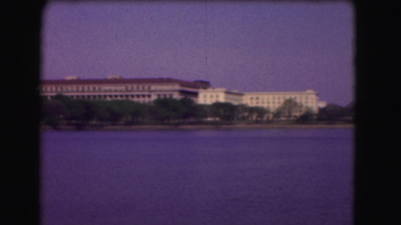 1975 Washington, DC 8mm frame showing a wide waterway with distant institutional buildings, trees, and purple-shifted sky.