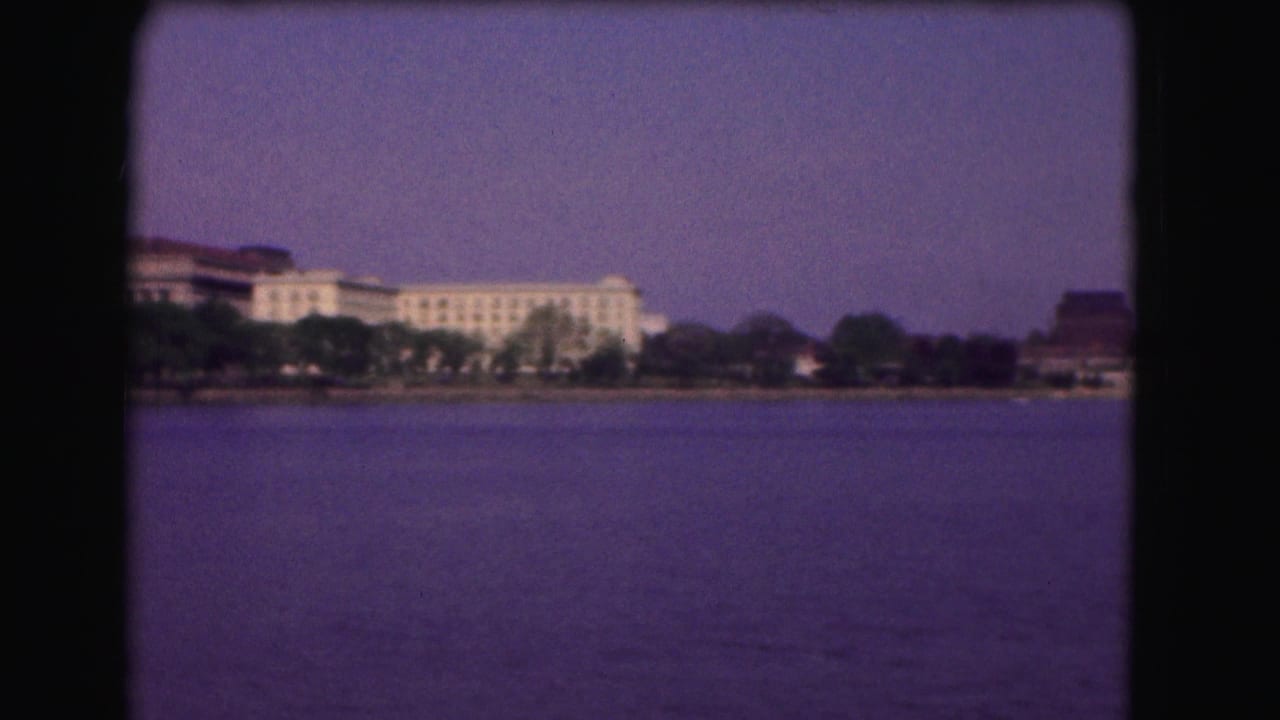 River view with far-shore buildings, trees, and open sky framed by black film borders.