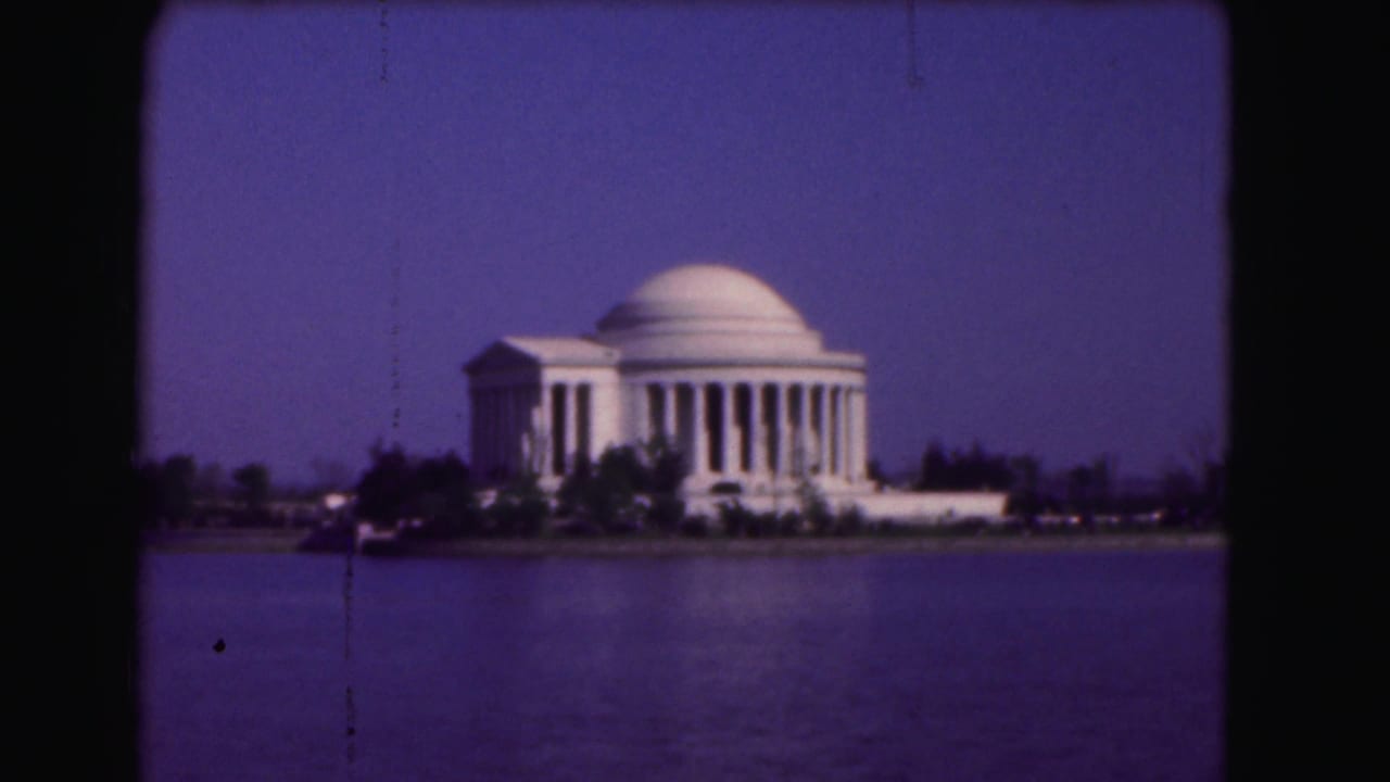 1975 8mm view of the Jefferson Memorial in Washington, DC, across calm water under a deep blue-purple sky.