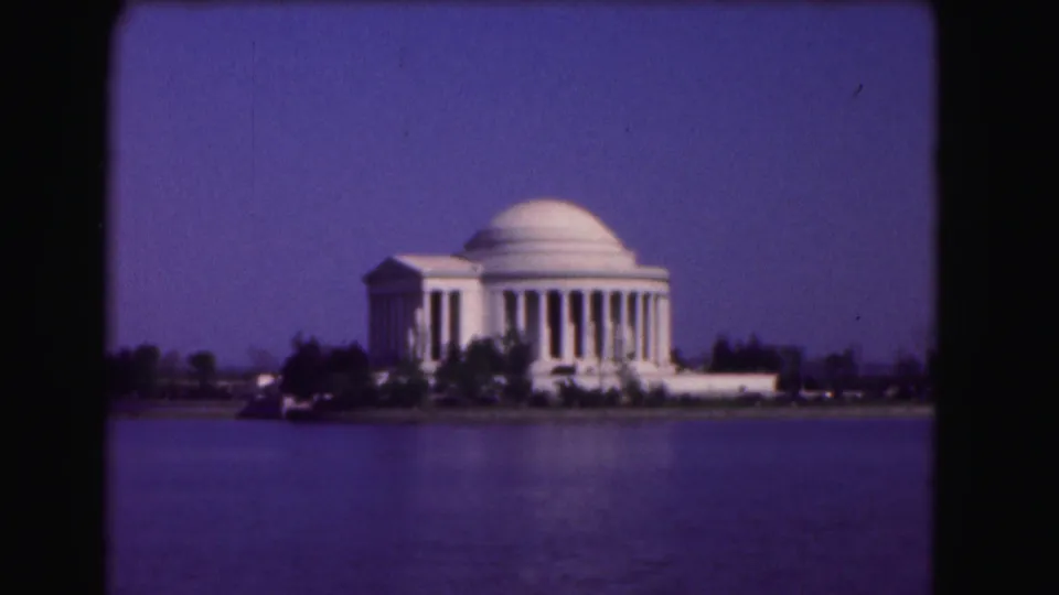 Steady 8mm frame of the Jefferson Memorial across the Tidal Basin, with soft focus and saturated blue sky.