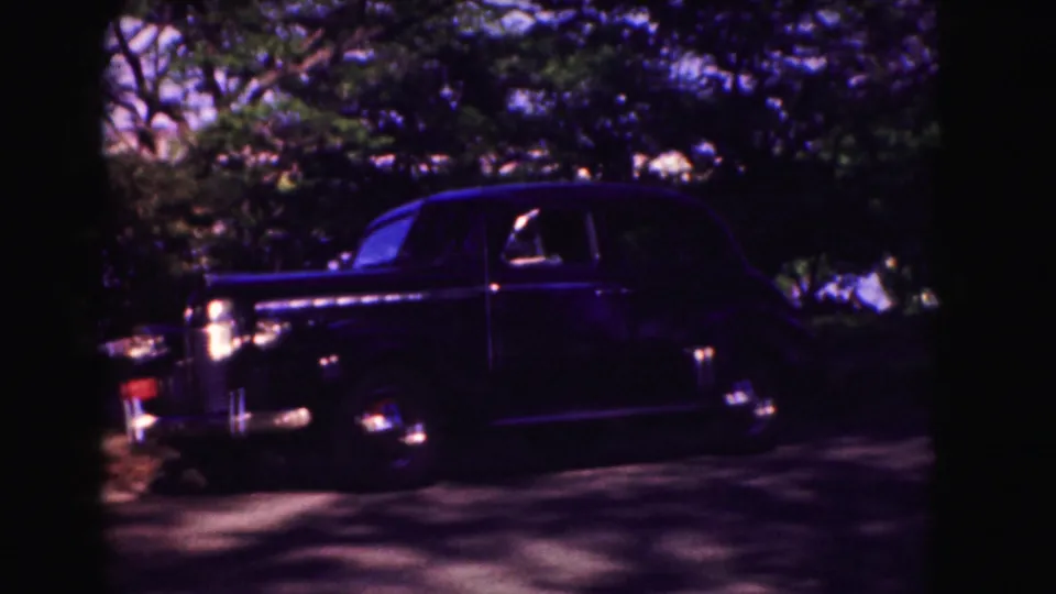 Dark mid-century American sedan parked beneath trees, filmed in soft, saturated 8mm color during the 1975 Washington, DC reel.