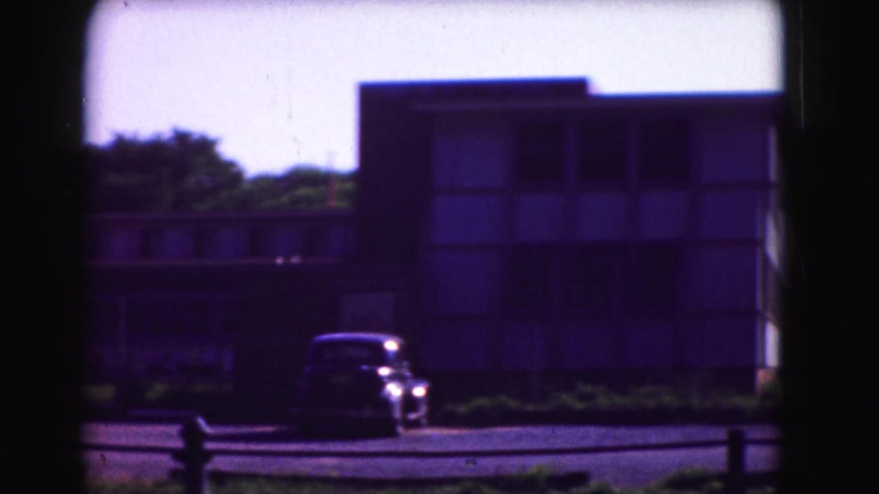 Older car parked in front of a rectangular building under bright sky.