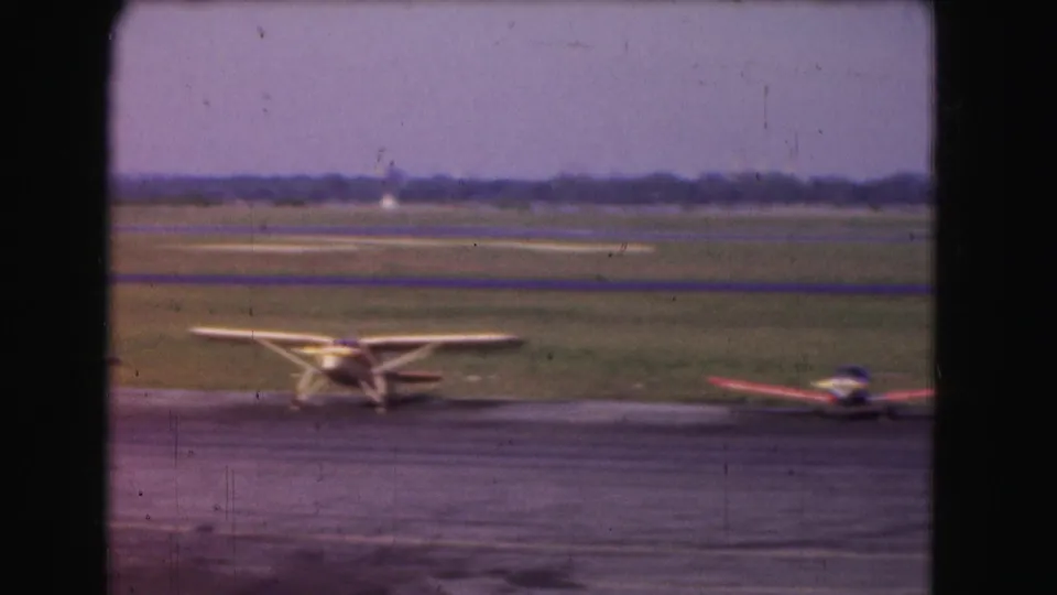 1975 Washington, DC home-movie frame showing a yellow high-wing propeller plane near another small aircraft on the tarmac.
