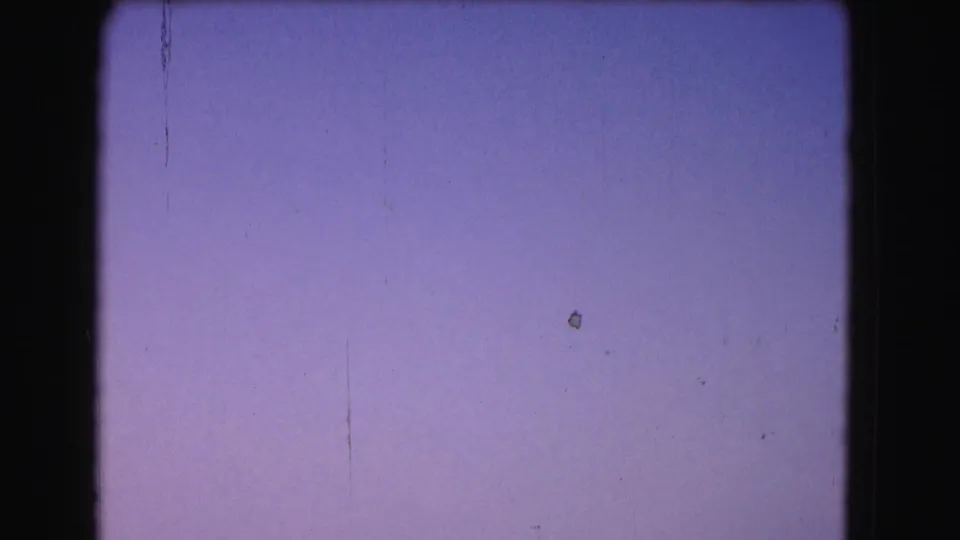 Final 1975 Washington, DC frame showing mostly clear sky, with film grain, dust marks, and a dark frame edge visible.