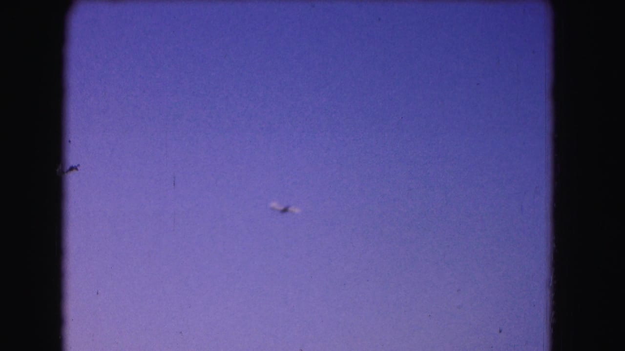 Tiny airplane in a blue-purple sky with visible film gate edges and dust.
