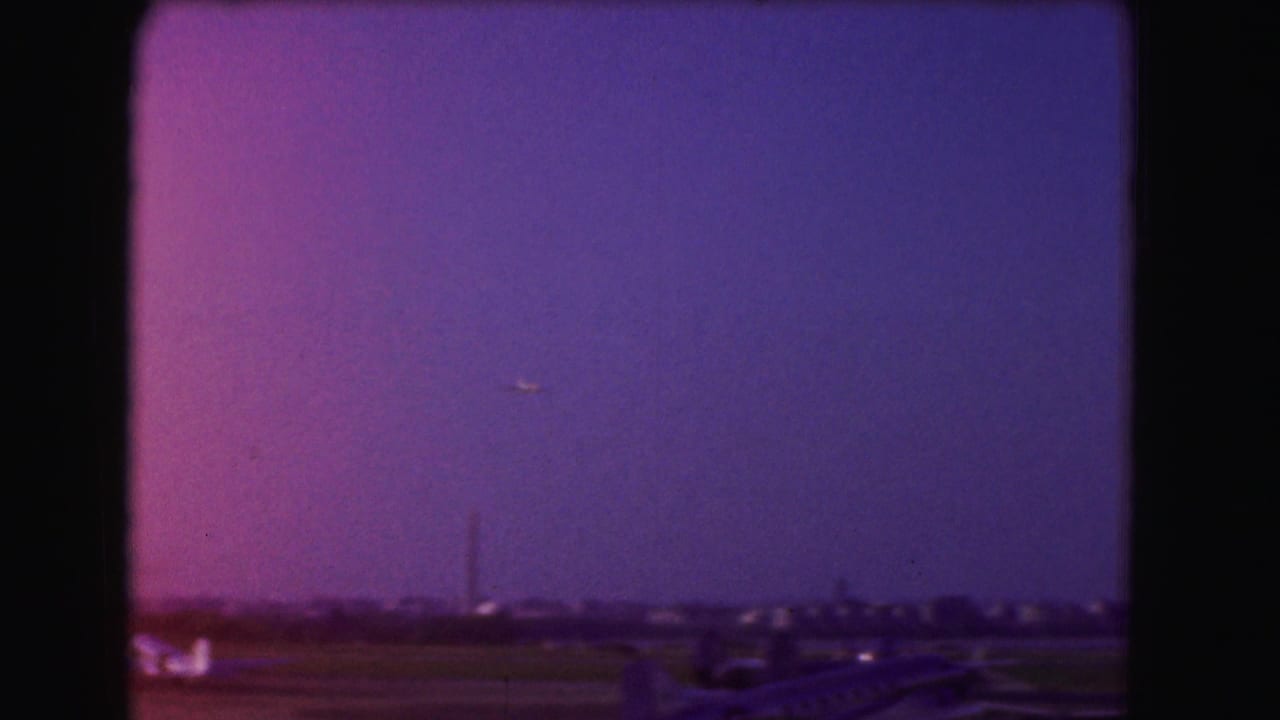 Small airplane above a runway horizon under a purple dusk sky.