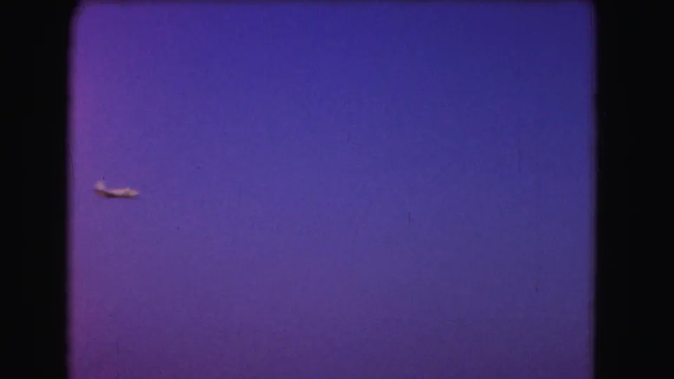 Small plane in flight against an open twilight sky in 1975 Washington DC home-movie footage.