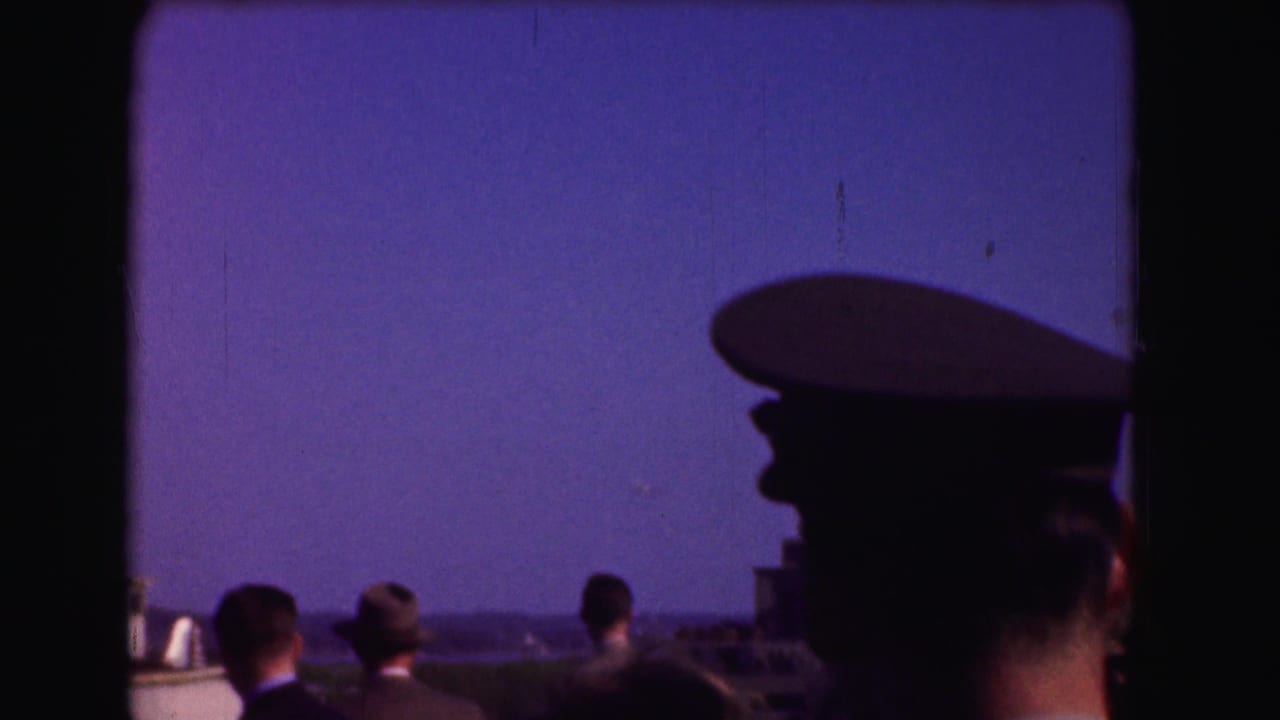 Silhouetted spectators look toward the sky beside a man in a military-style cap.