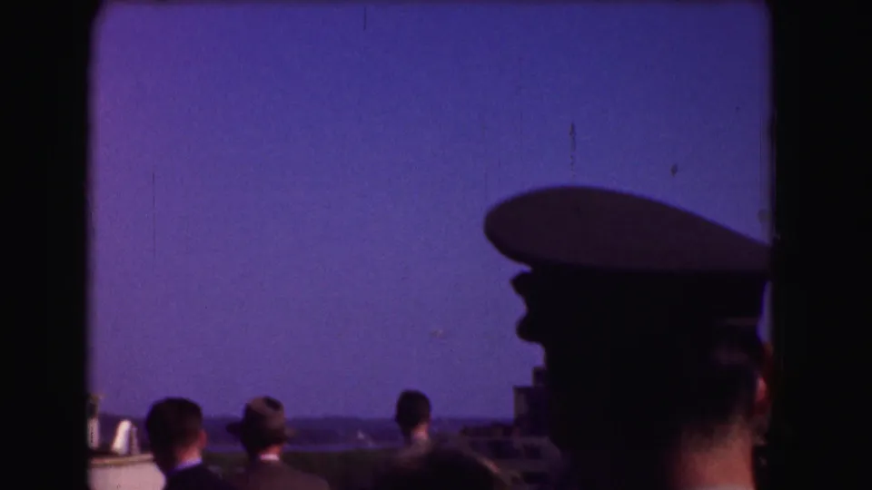 1975 Washington DC home-movie frame with silhouetted spectators and a man in a military-style cap looking toward the sky.