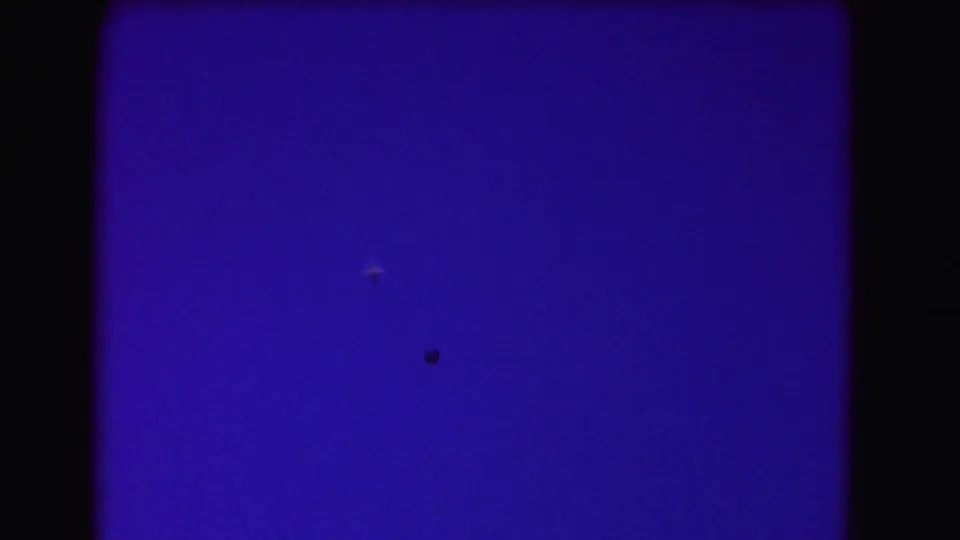 A tiny aircraft crosses a saturated blue 8mm frame, with no ground detail visible.