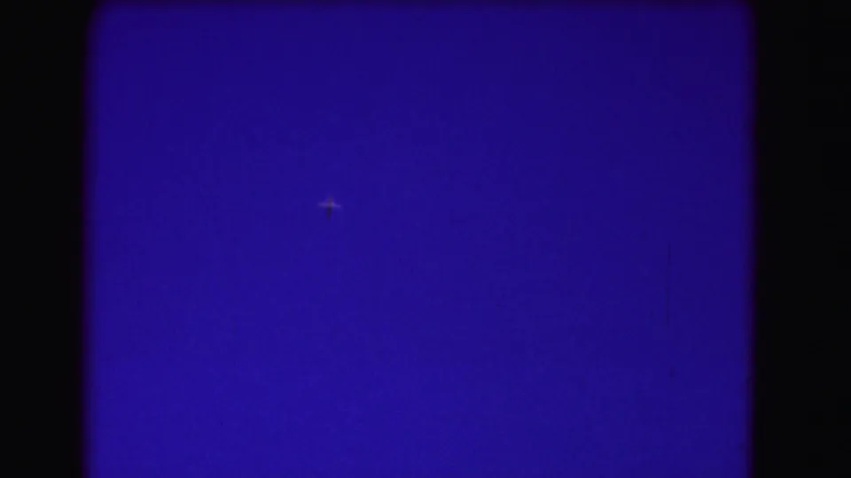 The distant aircraft remains small against the saturated blue sky in this 1975 8mm home-movie frame.