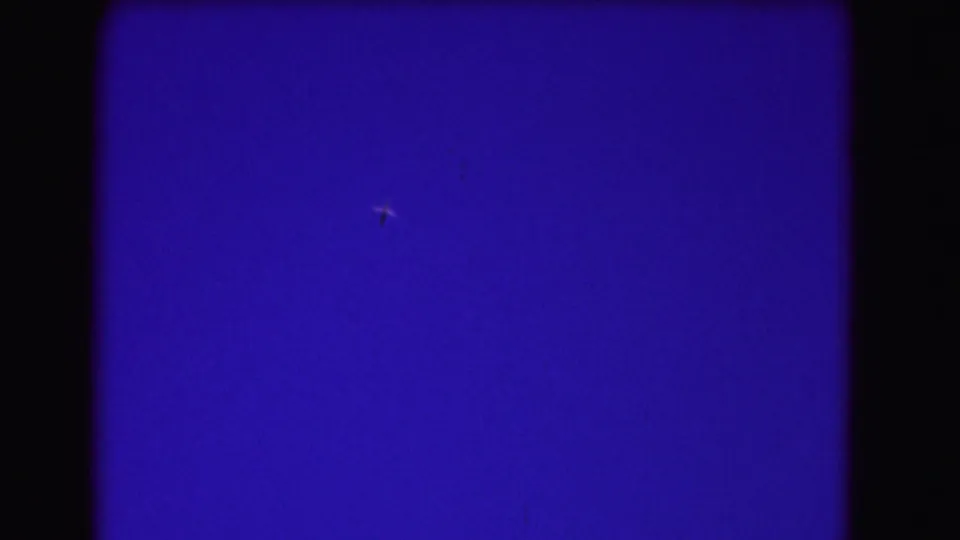 A distant aircraft moves through a blue sky frame, with visible grain and rounded 8mm borders.