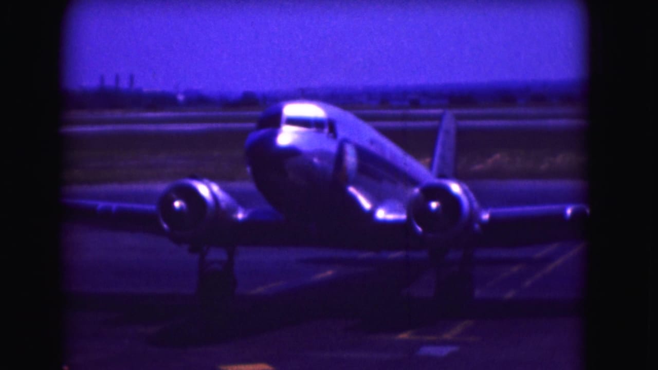 Propeller aircraft centered on the tarmac, framed by black film edges.