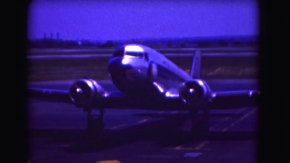 1975 Washington DC frame with a reflective twin-engine aircraft moving along the runway in soft, blue-purple small-gauge film color.