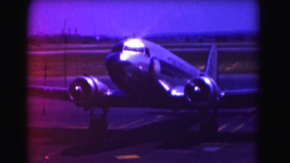 1975 Washington DC frame showing the aircraft taxiing on the runway, with magenta-blue color shift, grain, and vertical film marks visible.