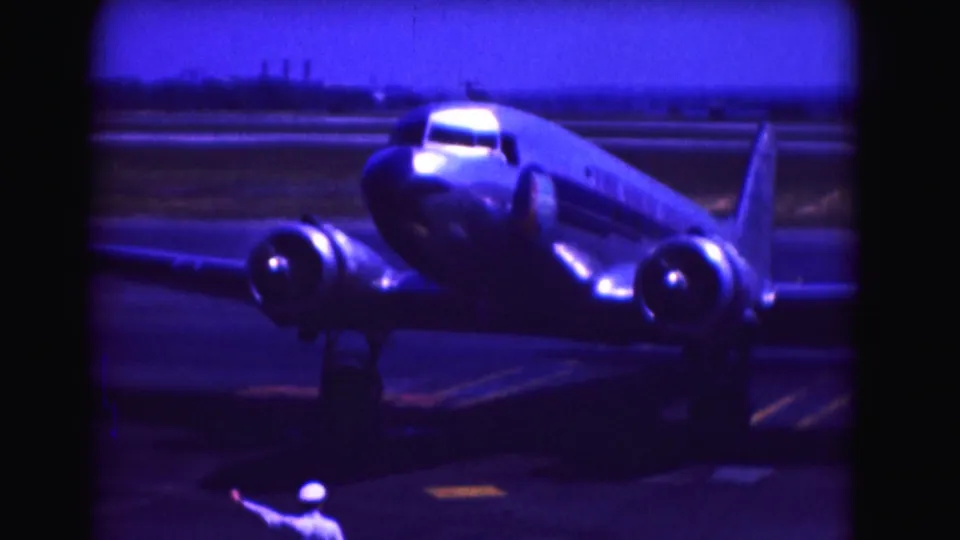 1975 Washington, DC-area frame with a ground crew member in white directing a propeller airplane as it turns on the airport tarmac.
