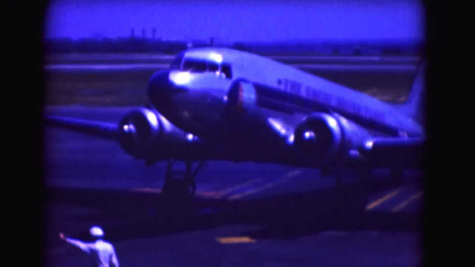 1975 Washington, DC-area 8mm frame showing a propeller aircraft turning while a ground crew member gestures from the foreground.