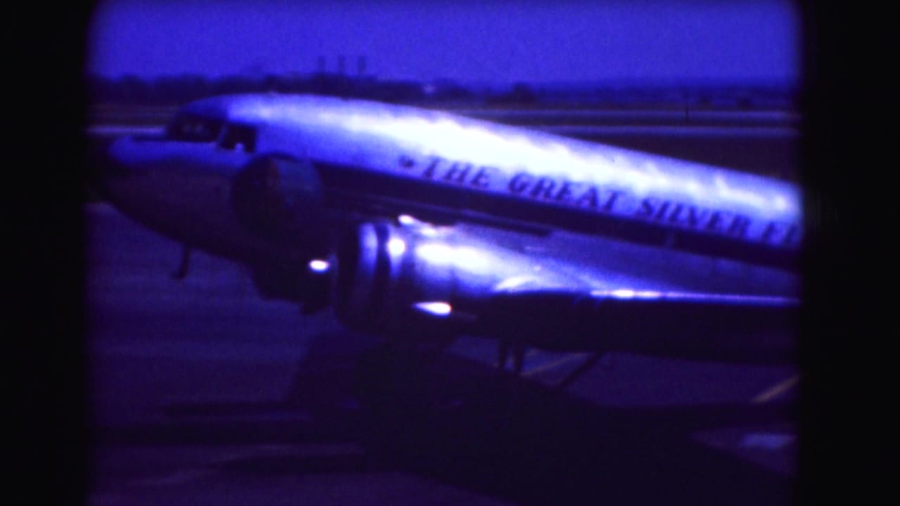 Propeller aircraft on a runway with fuselage lettering visible in blue-tinted 8mm footage.