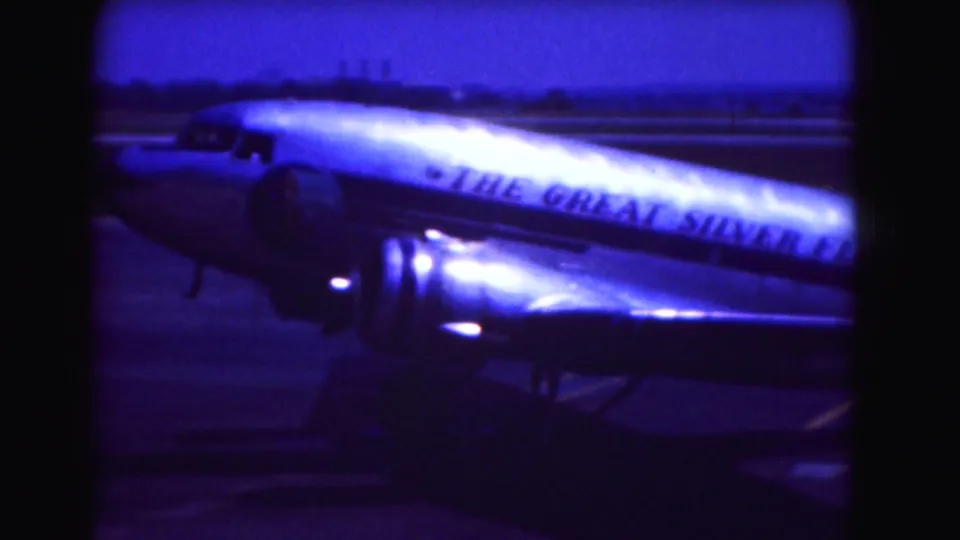 1975 Washington DC home-movie frame showing a propeller passenger aircraft on the tarmac with visible fuselage lettering.