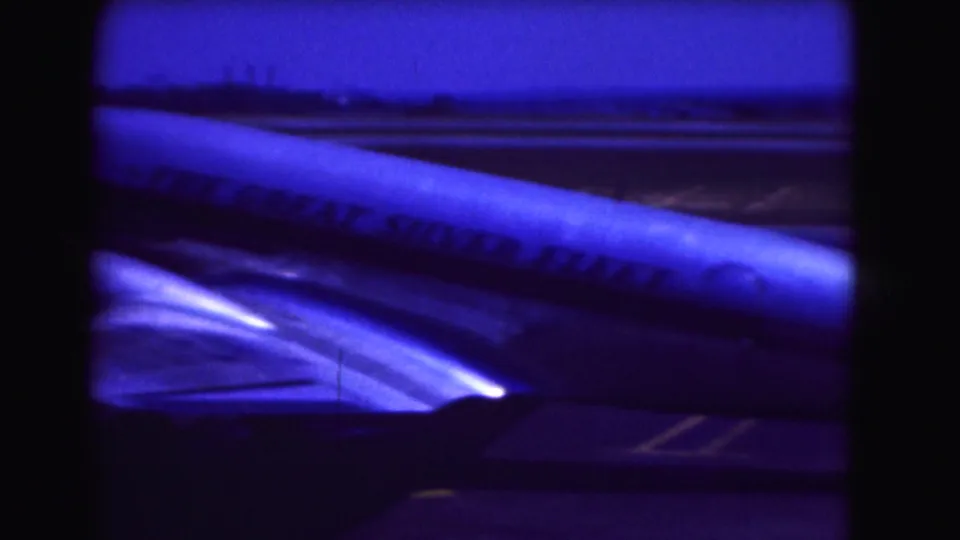 Blue-shifted 8mm frame from the Washington DC airport clip showing the aircraft fuselage, wing, and partial slogan lettering.