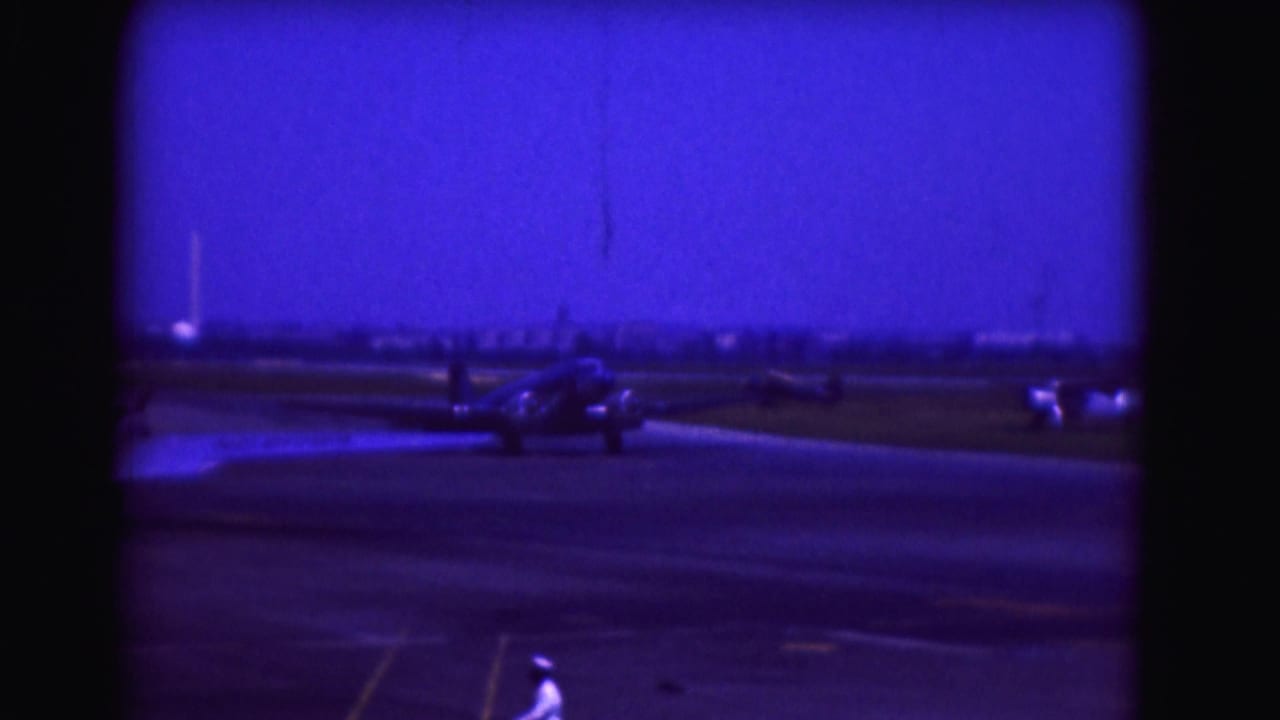 Small propeller aircraft centered on a runway with a person in white at the lower edge.