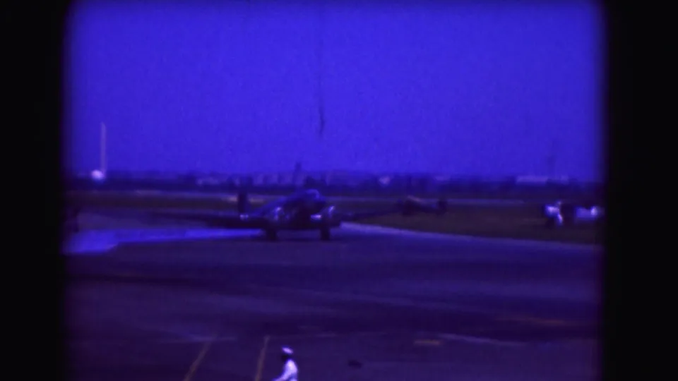 1975 Washington DC airport view showing a propeller aircraft taxiing under a deep blue sky, with a foreground figure partly visible.