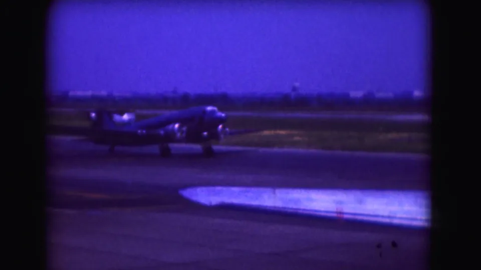 1975 Washington, DC airport frame with a taxiing propeller airplane and a foreground wing edge under a saturated blue sky.
