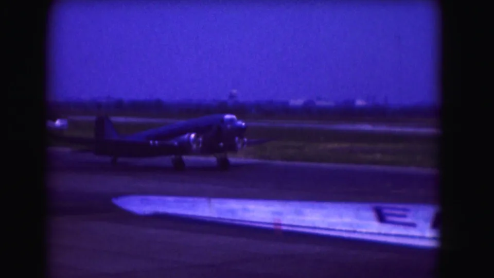 Blue 8mm home-movie frame of a propeller airplane on the runway behind a foreground wing, supported by 1975 Washington, DC metadata.