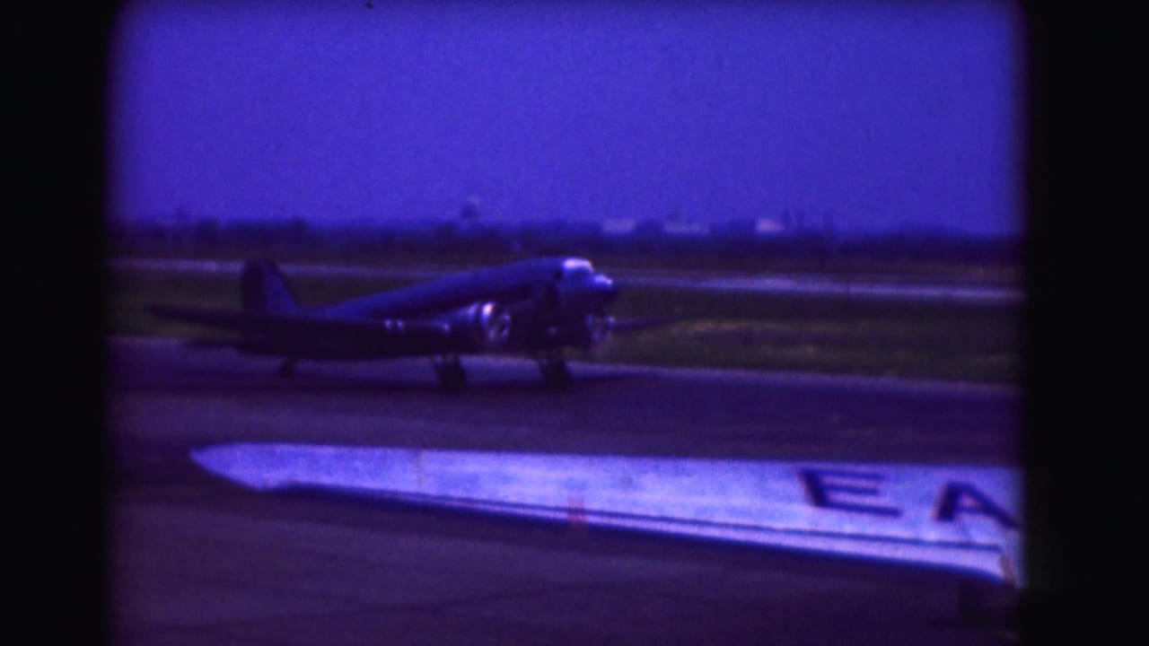 1975 Washington, DC-area home-movie frame showing a propeller airplane on the tarmac, seen past a foreground aircraft wing.